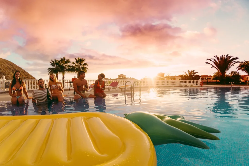 Grupo de amigos felices en una piscina con la puesta de sol de fondo